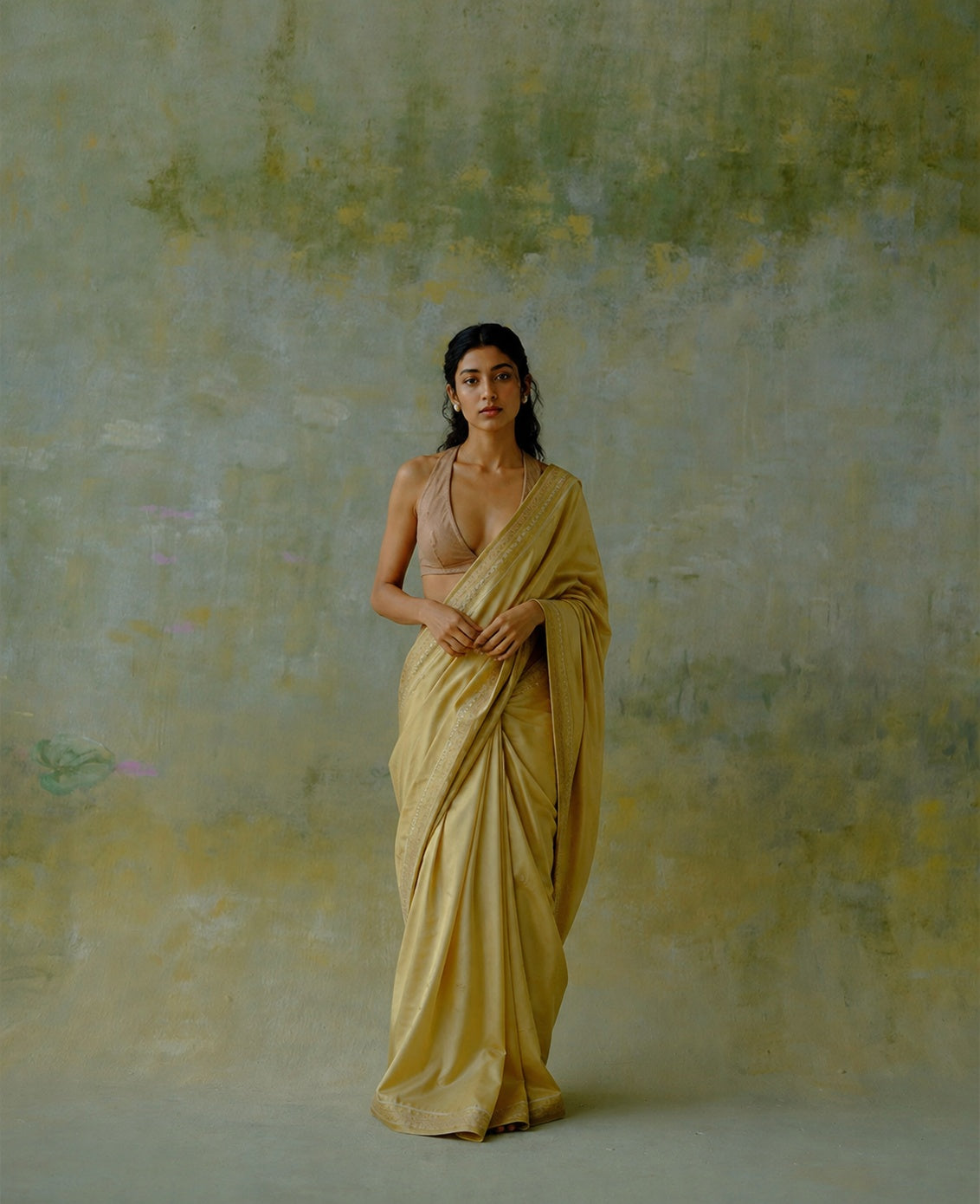 Aadya saree model in gold sari against a textured neutral background